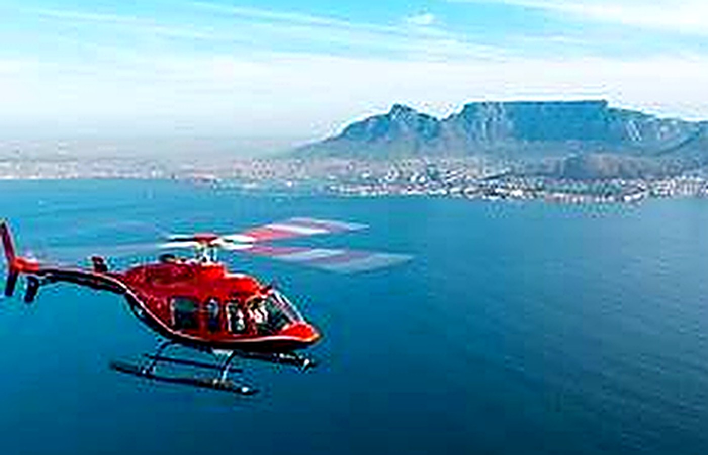 Red helicopter flying over Cape Town with Table Mountain behind